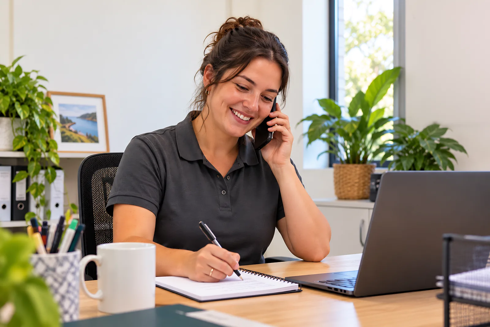 Finding Path team member smiling while taking notes during a phone call at her desk